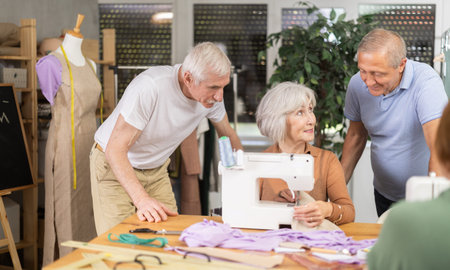 Senior female teacher demonstrates technique sewing with machine, shares skills with elderly...