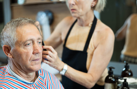 Elderly man getting haircutting by female barber using clipper in barbershop
