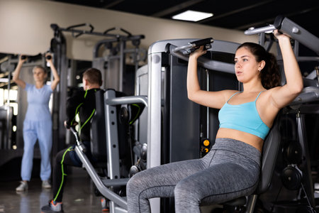 Girl performing shoulders press in exercise machine in gym