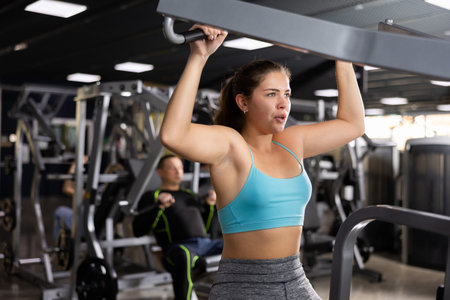 Young woman trains her arm muscles using a simulator in gym