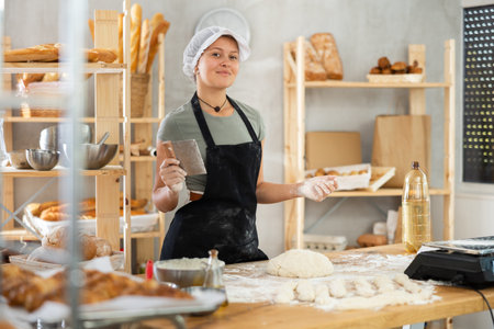 Young baker girl is standing near work table in kitchen, working with dough