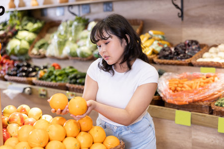 Happy smiling teenage girl making purchases in supermarket, choosing fresh orangesの写真素材