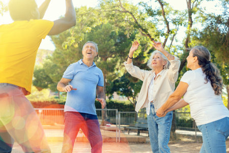 Joyful multiracial group of mature adult people playing volleyball game outdoorsの写真素材