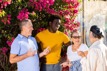 Mature multinational cheerful males and females talking outdoors near the park on a sunny dayの写真素材