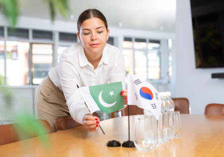 Female employee of the delegation sets flags of countries of South Korea and Pakistan on the table...