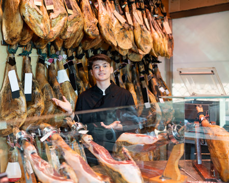 Male seller cutting slices from whole leg of jamon in meat store