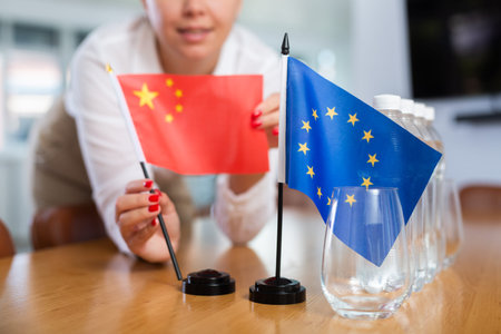 Female secretary places flags of the European Union and China flag on the table before negotiations...
