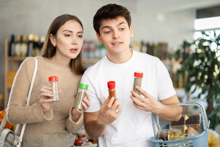Pretty young wife tells her husband what delicious spices and seasonings to buy in supermarketの写真素材