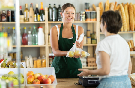 Young woman seller weighs apples in bagの写真素材