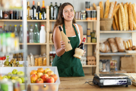Young female seller offering wine in grocery storeの写真素材