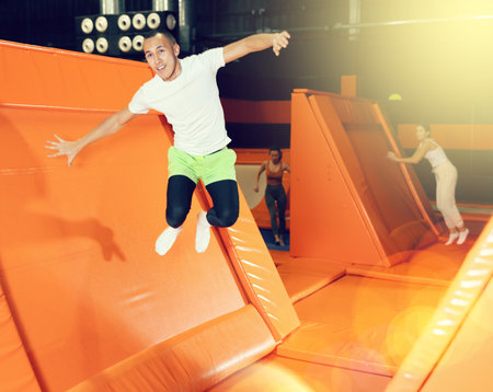 Excited man pushing off from inclined surface in indoor trampoline centerの写真素材