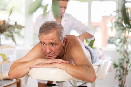 Relaxed old man having back massage therapy conducted by skilled masseuseの写真素材