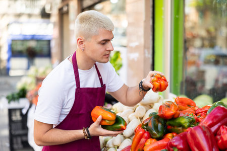 Young guy seller puts peppers in vegetable shop
