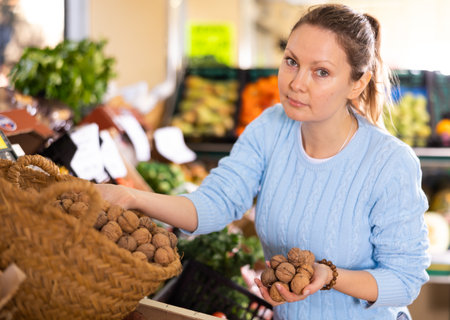 Portrait of busy middle-aged European woman buying walnuts in shell in grocery storeの写真素材