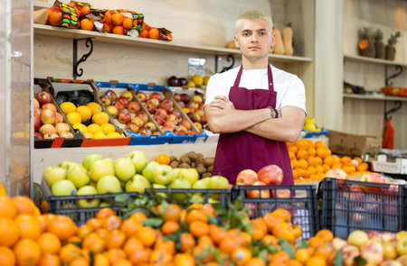Young man seller in apron stands in trading hall in vegetable storeの写真素材