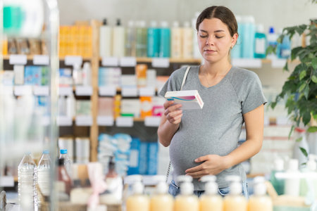 Portrait of attentive pregnant woman holding and choosing box with best pills to improve well-being in pharmacyの写真素材