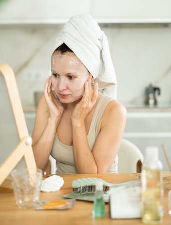 Woman with towel head wrap applying cosmetic face mask