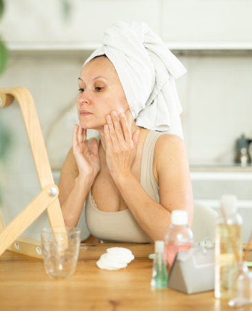 Woman with hair wrapped in towel inspecting complexion in mirrorの写真素材