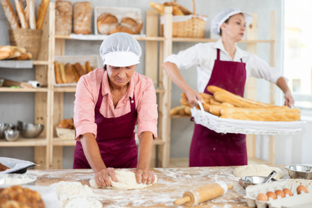Aged woman baker kneading dough in artisan bakery