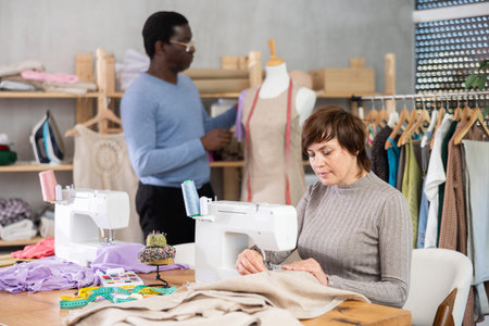 Female seamstress stitching on sewing machine in workshop with colleague