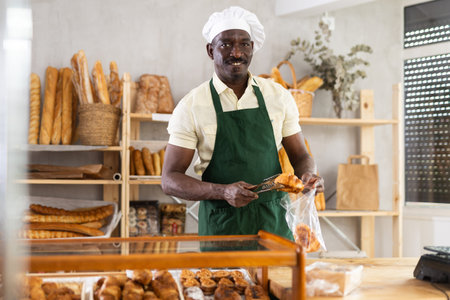 Male baker putting hot delicious croissants in plastic bag for sale