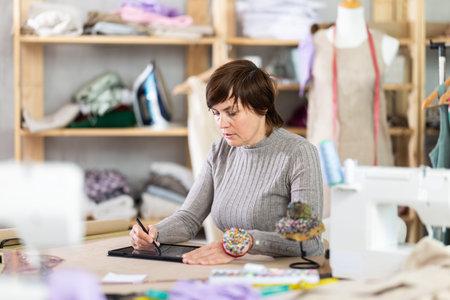 Female tailor designing custom dress using tablet in studio