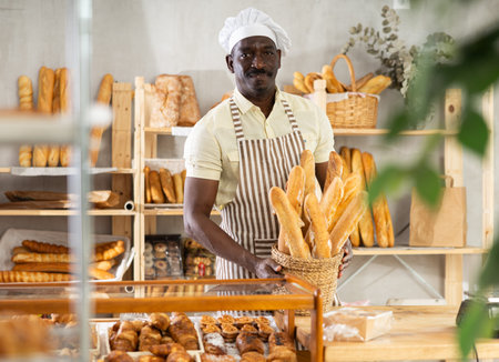 African male baker worker sells baguette, shows many products