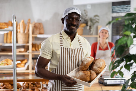 Portrait of male baker with bread and baguettes in hands in bakery