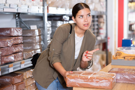 In specialized store, woman chooses and buys briquettes with red clay