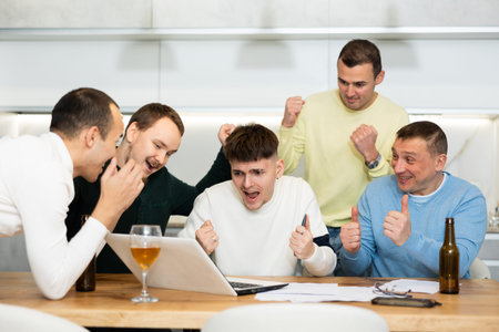 Group of friends watching football match on a laptop together and drinking beer