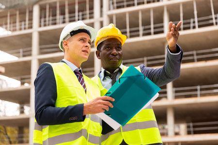African-american engineer discussing a construction plan with a colleague shows him something