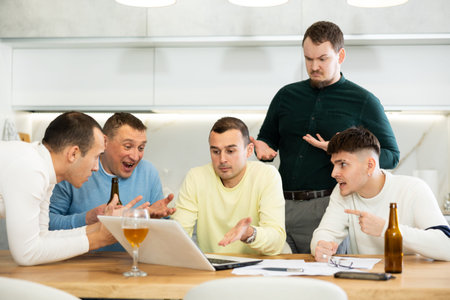 Group of male friends solving problems using laptop and drinking beer