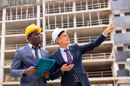 Young architect discussing a construction plan with a colleague points to something