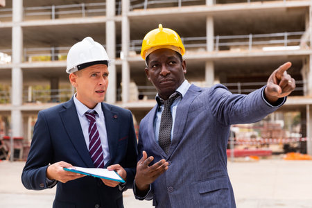 Positive architect and contractor having brief meeting on construction site