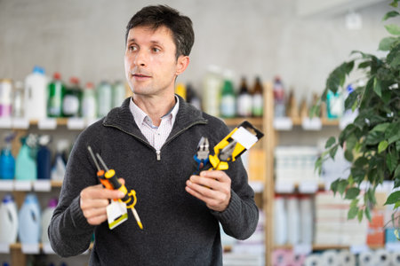 Attentive man selects various tools - screwdrivers, pliers for repairs in supermarket