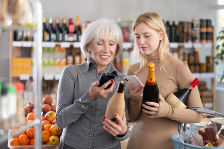 Girl and grandmother scan QR code, take reading wine and champagne label using phone camera in shopの写真素材
