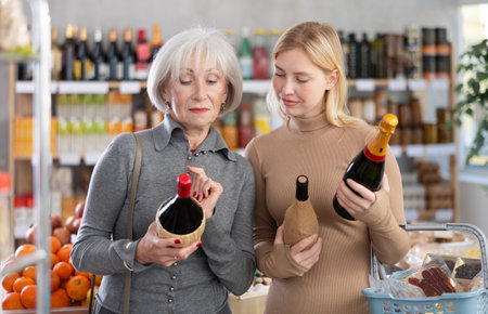Shopping in produce supermarket - two female buyer makes choice bottle of wineの写真素材