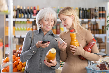 Elderly mother and her adult daughter scan a QR code on a tomato and peach juice label together to...