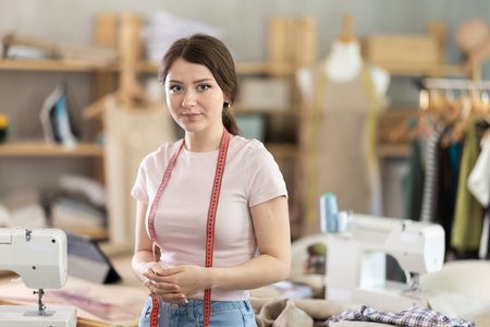 Portrait of positive girl tailor in sewing workshop