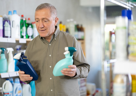Male shopper carefully selects a spray glass cleaner for windows in homeのeditorial素材