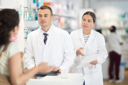 Male and female pharmacists speaking to woman customer buying medical preparation in drugstoreの写真素材