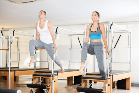 Young man and woman performing Pilates exercises on Wunda chairs