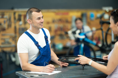 Bicycle technician writing repair checklist and discussing with female client