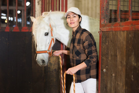 Woman holding rein and leading horse out of stable