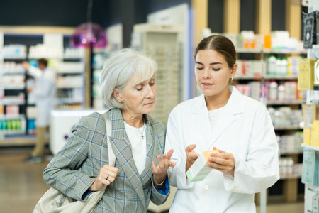 Young female pharmacist consulting old costumer about care product in boxの写真素材