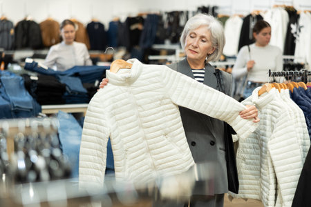 Old woman choosing white jacket in clothing storeの写真素材