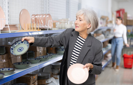 Smiling elderly woman choosing ceramic Asian style plates in storeの写真素材