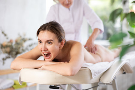 Young woman suffers painful sensations and winces during therapeutic massage sessionの写真素材
