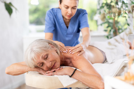 Smiling senior woman lying on couch during back massageの写真素材