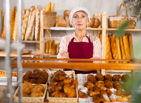 Senior female baker worker sells croissants, shows many different âcrescent rollsの写真素材